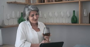 Senior old attractive woman using tablet for video call, drinking wine and participating in a chat with children, participating in family distant party celebration, active leisure feeling alone
