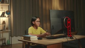 Asian Girl Learning Online With Desktop Computer From Home, She Turns And Warmly Smiles Into The Camera
