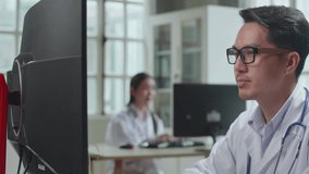 Asian Male Doctor Communicates With Patient By Video Link, Doctor Consults Patient Using Modern Technologies, Using Desktop Computer In Workplace
