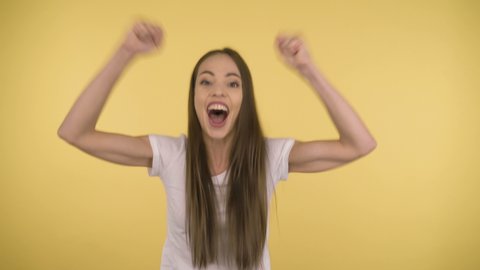 Adult Attractive Lady 35 years old dressed in a white T-shirt sincerely rejoices with good news or overhaul at the studio on an isolated yellow background.