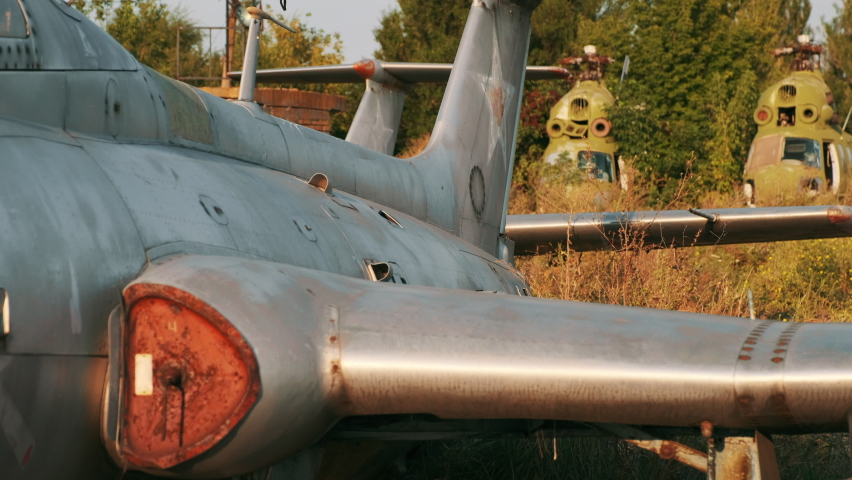 Old  training airplanes with grey rusty fuselage made in USSR against helicopters on abandoned aerodrome at sunset light