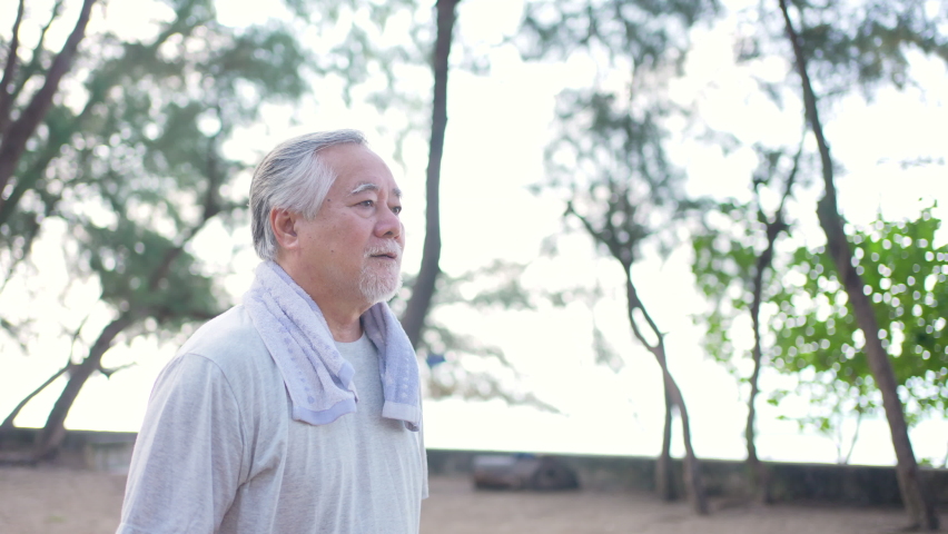 4K Healthy Asian senior man in sportswear jogging exercise at the beach in summer morning. Wellness elderly retired man enjoy outdoor lifestyle activity and sport training workout for good health.