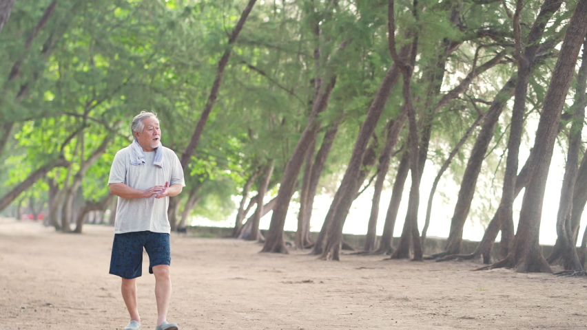 4K Healthy Asian senior man in sportswear jogging exercise at the beach in summer morning. Wellness elderly retired man enjoy outdoor lifestyle activity and sport training workout for good health.