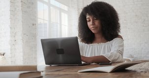 Thoughtful young black businesswoman brunette typing on laptop and answering mobile call. Focused female writing news article, browsing social media, distancte internet job concept.