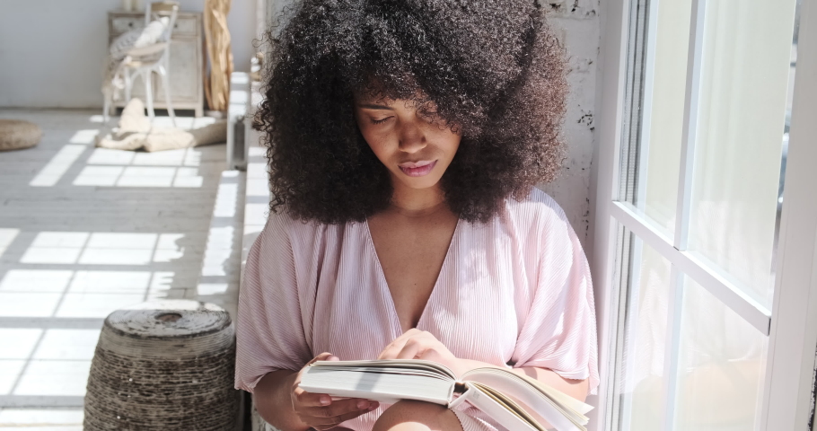 A young mixed race woman is carefully reading an interesting book, a fiction, a novel, thinking about what he was reading. A quiet day at home without electronic gadgets or mobile phones. Royalty-Free Stock Footage #1078898174