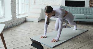Athletic young woman watching video tutorial on tablet doing exercises at home with large windows in morning. Watch instructional sports classes, online training workout concept, fitness app.