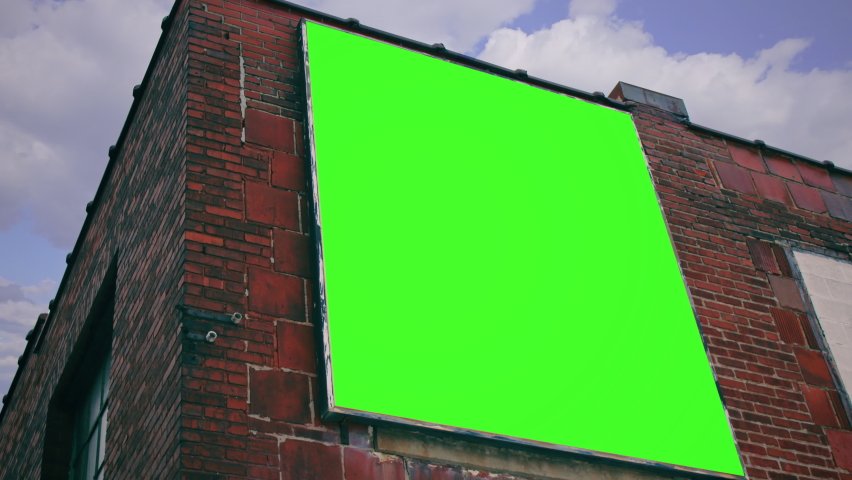 Building Billboard Green Screen Tilt Up Panel Cloudy Sky. A large billboard with a green screen on a building wall under a cloudy sky. Tilt up Royalty-Free Stock Footage #1078900490