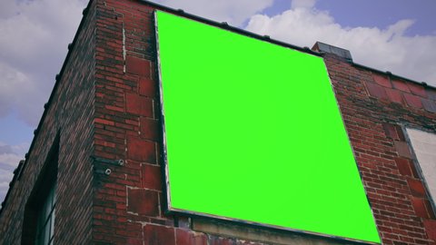 Building Billboard Green Screen Tilt Up Panel Cloudy Sky. A large billboard with a green screen on a building wall under a cloudy sky. Tilt up