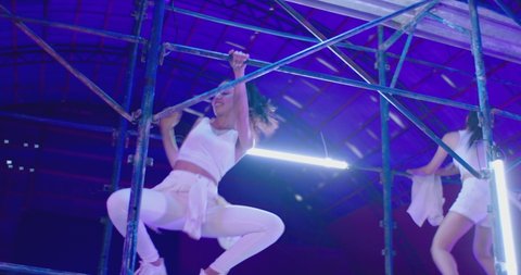 Many female dancers dressed in white shorts dancing inside abandoned building in high scaffolding construction . Stylish Girls dancing, twerking , doing gymnastic movements , jumping . Slow motion 

