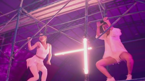 Many female dancers dressed in white shorts dancing inside abandoned building in high multistage  construction . Stylish Girls dancing, twerking , doing gymnastic movements , jumping . Slow motion 
