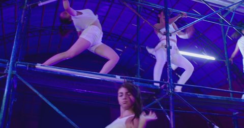 Many female dancers dressed in white shorts dancing inside abandoned building in high scaffolding construction . Stylish Girls dancing, twerking , doing gymnastic movements , jumping . Slow motion 

