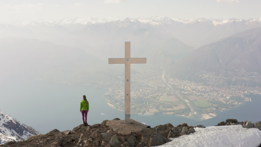 Drone aerial shot of young woman hiking reaching the mountain top. Spectacular views of lake and mountain, female on a hike. Shot with a drone 