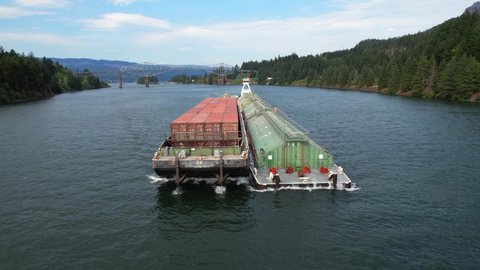 Long river barge travelling down a wide river in the Pacific Northwest. Drone video up close to container ship flying backwards.