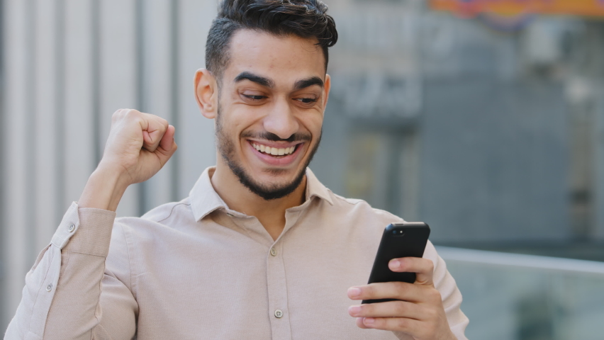 Hispanic amazed businessman receiving sms message offer opportunity, arabian happy man reading good news in smartphone. Excited overjoyed male winner outdoors celebrating success mobile phone victory Royalty-Free Stock Footage #1078916696