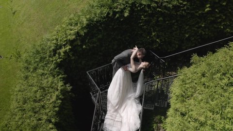 Newlyweds. Lovely young caucasian bride and groom on stairs in park. Happy wedding couple. Woman walking to man. Summer. Bride in gorgeous luxury wedding dress. Bridegroom in love. Aerial drone view
