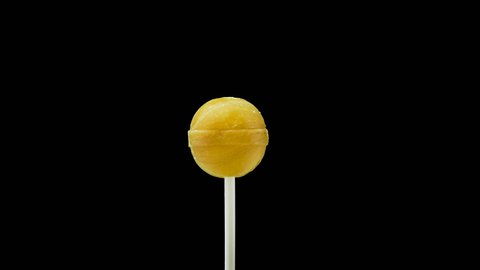 Yellow lollipop rotates on a stick on a black background. Children's candy. Background for music