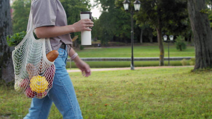 Woman walking and carrying white mesh string knitted shopping bag with groceries and drinking from reusable metal cup. Eco friendly, reusable shopping bag. Zero waste and plastic free concept. | Shutterstock HD Video #1078928369