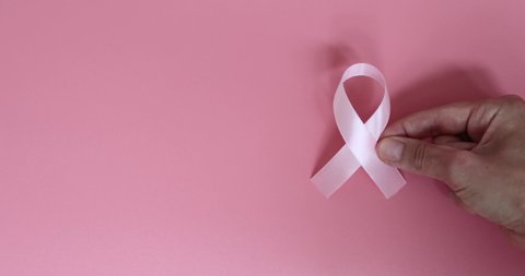 Pink breast cancer awareness ribbon and hand on pink background. Slow motion.