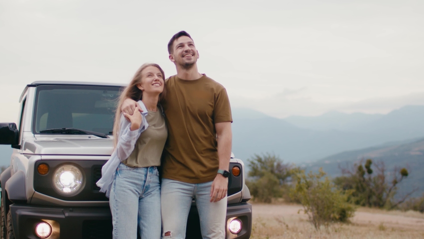 Young traveler couple on road trip in mountains standing near car
