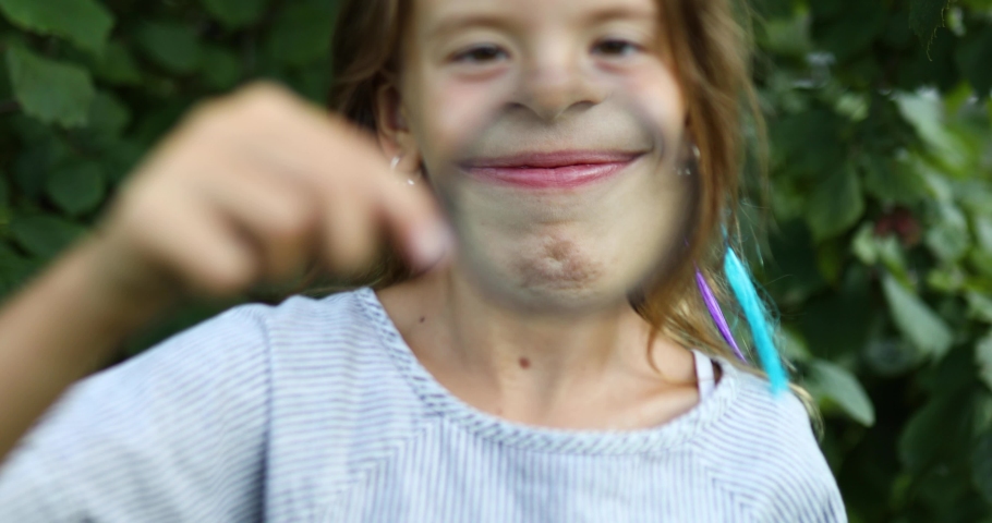 Little girl playing with a magnifying glass in her backyard make faces. Childhood lifestyle concept, Education, school concept