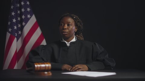 Black female judge listening to witness talking in court room, justice system