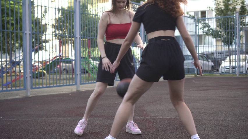 Two young active women play basketball on a sports basketball street court. Sports youth.