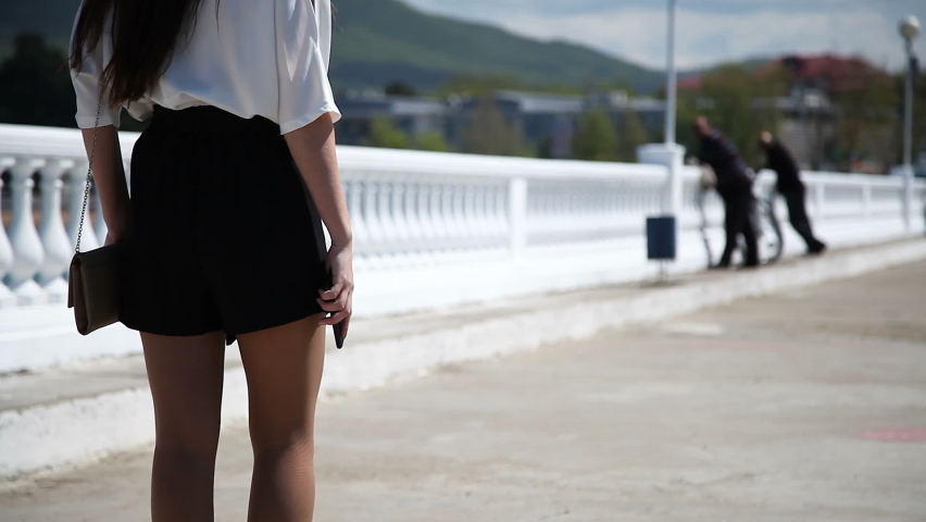 A girl in shorts and heels walks along the balustrade with a phone in her hand