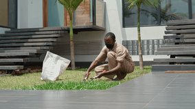 dark-skinned gardener mows the lawn with a pruner