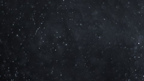 White-silver particles in the air on a black background. Some of the particles are blurred in a beautiful bokeh. 4K background for your videos in various mixing modes.