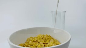 Milk pouring into glass and corn flakes in blow slow motion, healthy cereal breakfast on white background