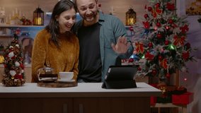 Couple using tablet for online video call on christmas eve. Man and woman chatting to family on conference via internet for holiday season celebration. Festive people in xmas decorated home