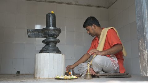 Howrah, West Bengal, India - 26th October 2020 : Hindu priest worshipping lord Shiva by offering flowers and prayers to Shiv Linga, inside a Shiva Temple. Shiva is most worshipped Hindu God in India.