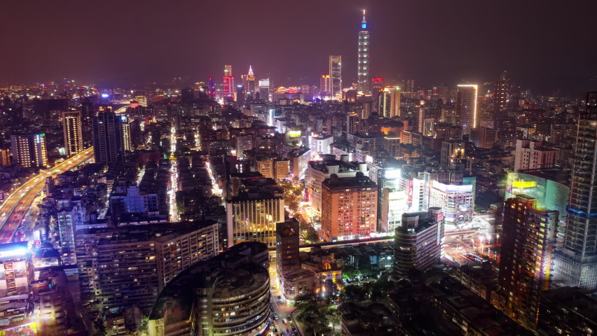 Night hyperlapse of Downtown Taipei, vibrant capital of Taiwan, with 101 Tower standing among modern skyscrapers in Xinyi District and car light trails dashing on an elevated expressway at rush hour