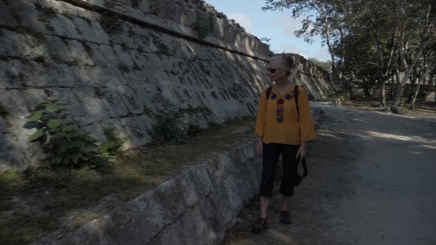 Mature blond woman walks among the ruins at Chichen Itza historical park in Yucatan, Mexico.