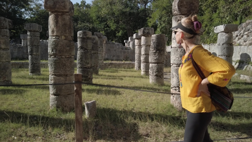 Mature blond woman walks among the ruins at Chichen Itza historical park in Yucatan, Mexico.