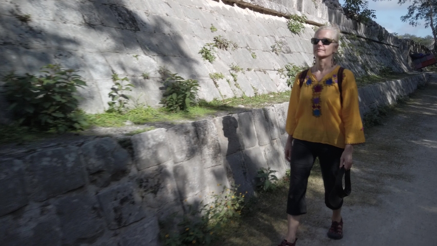 Mature blond woman walks among the ruins at Chichen Itza historical park in Yucatan, Mexico.