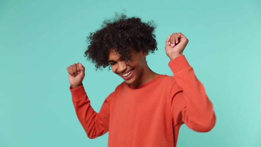 Slow motion fancy young curly african american man 20s wears azure t-shirt dance fool around have fun gesticulating with hand enjoy relax isolated on plain pastel light blue background studio portrait