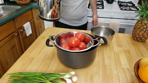Home cooking - pouring boiling water over tomatoes blanching them and getting ready for skin removal.