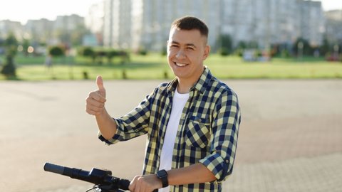 Caucasian hipster man leaning on electric scooter looking at camera and showing thumb up. Hipster man on vehicle outdoors. Eco-friendly modern urban transport. Ecology and urban lifestyle