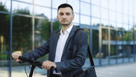 Portrait shot of caucasian man leaning on electric scooter and looking at camera. Stylysh man on vehicle outdoors. Eco-friendly modern urban transport