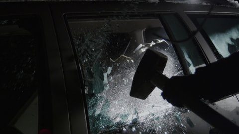 Smashing car window with sledge hammer, shattering glass of vehicle, slow motion