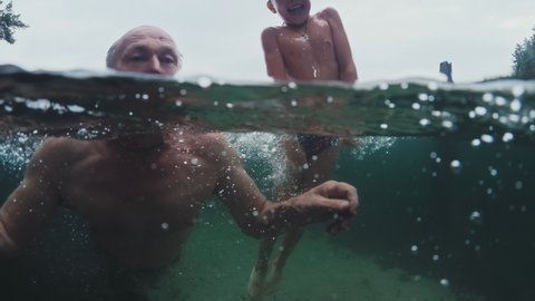 Family swim in lake. Preteen boy swims and has fun in the lake with grandfather. Underwater view of the family jumping and swimming in the lake