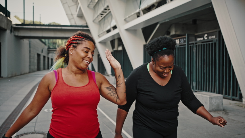 Two positive african american ladies going home after intensive cardio training, giving high five to each other and laughing, follow shot, slow motion Royalty-Free Stock Footage #1078975868