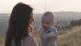 Mother holding cute baby in her arms on a walk outdoors, cute caucasian six month old baby boy, happy family embrace. High quality 4k footage