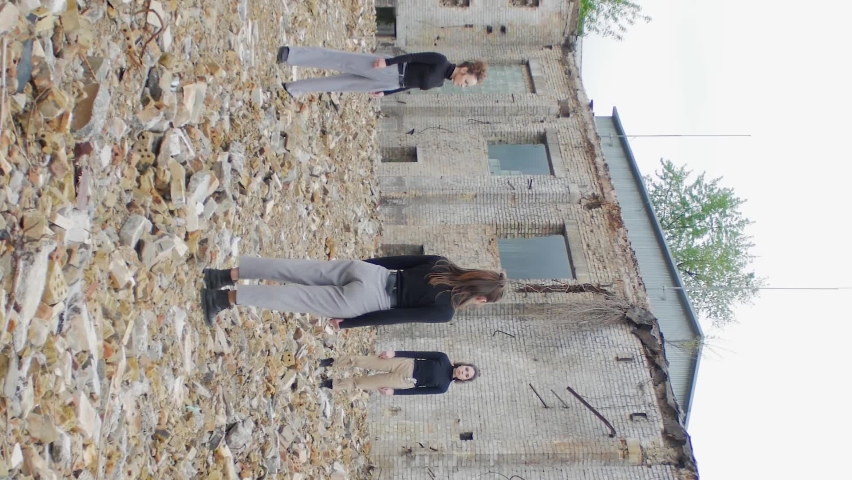 Vertical video of group of young people stand in the ruins of apocalypse post on the ground, Young woman in black are turned around against the background of a collapsed building and scattered bricks Royalty-Free Stock Footage #1078981028