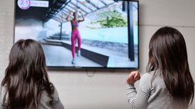 Little cute girls exercise watching online video via smart TV and doing fitness exercise dance at home. Happy Asian sisters spending time together on vacation.