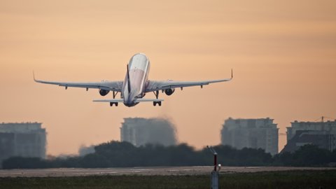 The plane takes off at sunset or sunrise. The wheels of the plane come off the runway of the airport.