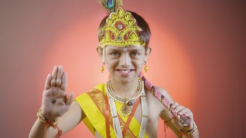 Smiling Indian boy in krishna fancy dress costume or attire blessing by looking into camera - kid during shri krishna janmashtami festival dressed like hindu god