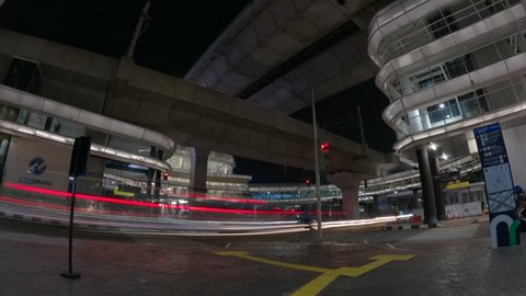 Jakarta, Indonesia - September 10, 2021: Timelapse of traffic under skybridge at CSW Integrated Transportation Stop with between Transjakarta bus and MRT train in the night. Wide angle, flat profile