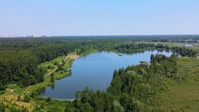 Flying over a forest lake with a wild beach. A sunny summer day. A lake with blue water. People on the shore relax and swim in the lake. The general plan. Shooting from a drone.